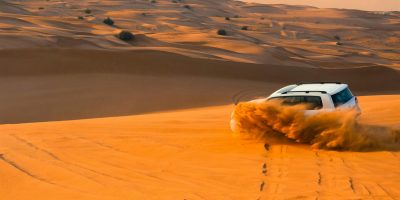A thrilling SUV driving through the sand dunes of Dubai's desert landscape at sunset.